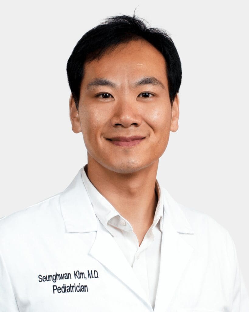 A man in white lab coat standing next to wall.