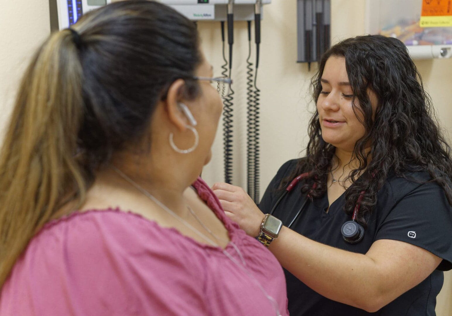 A woman is getting her stethoscope adjusted by another person.